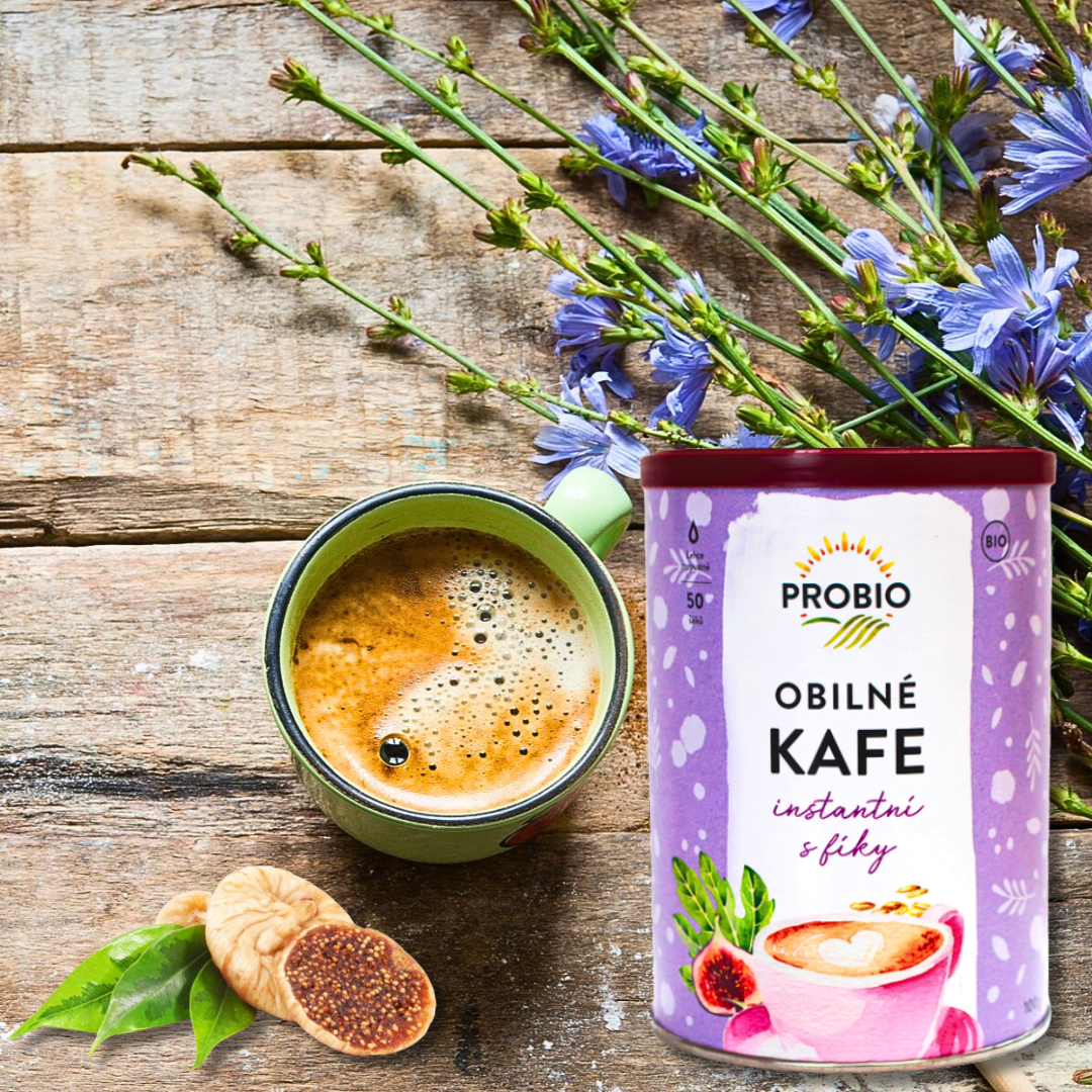 PROBIO “Obilné kafe instantní s fíky” tin next to a mug of coffee-like drink and figs on a rustic wooden table with blue chicory flowers.